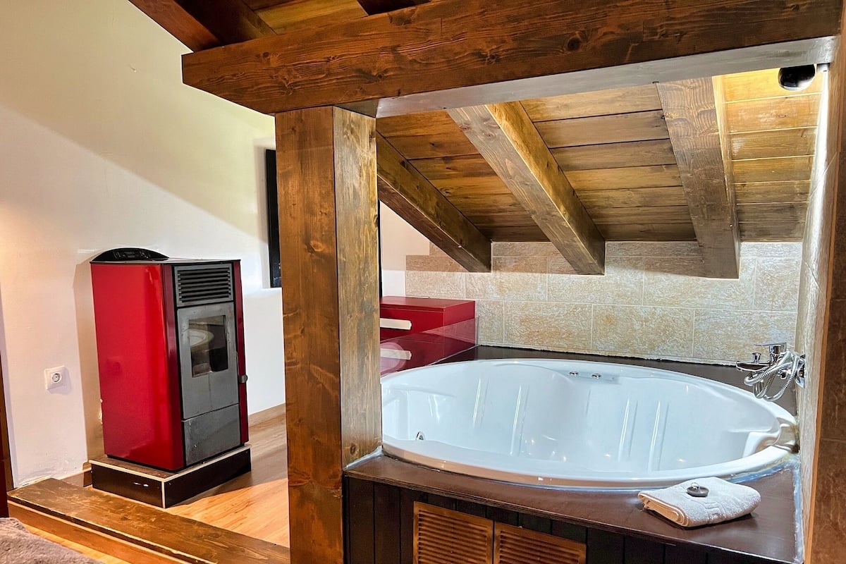 Un baño con una bañera grande, vigas de madera y un electrodoméstico rojo.