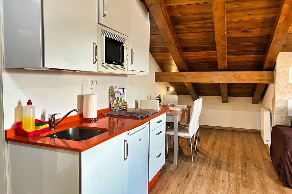 Una cocina compacta con armarios blancos, microondas y techo de madera.