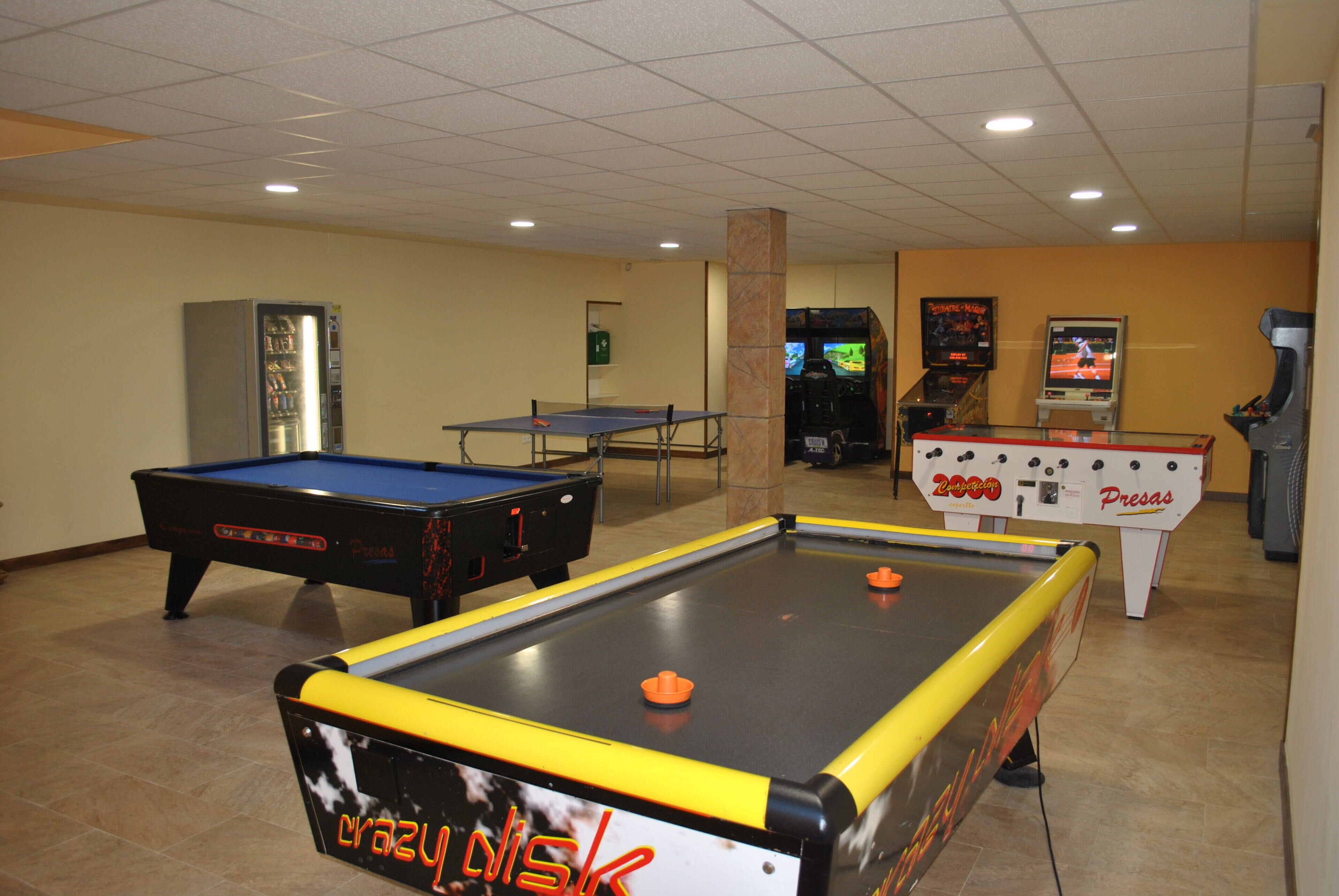 A pool table, a foosball table, and a ping pong table in a room with tiled floors and a tiled ceiling.