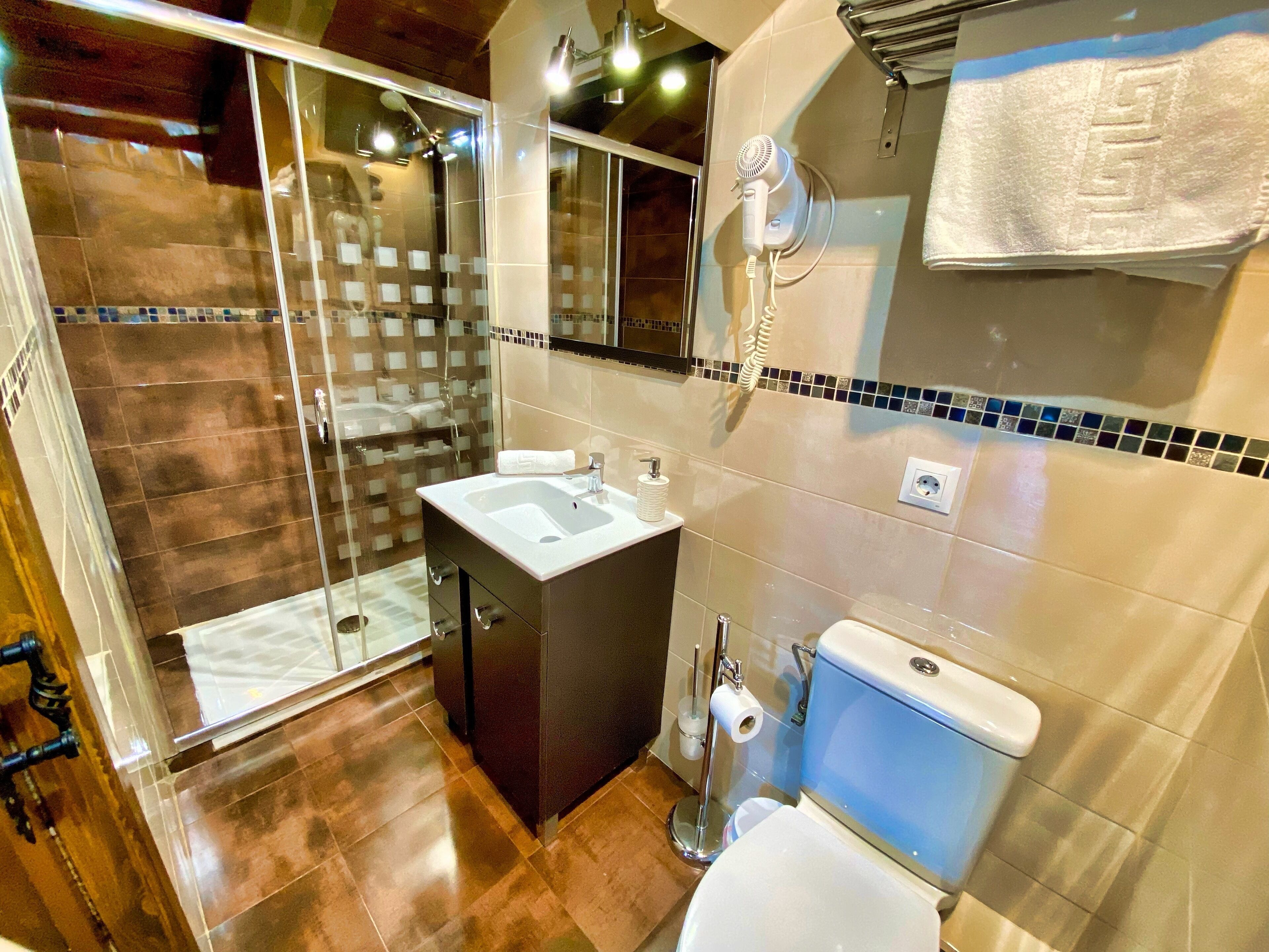 Un baño moderno con ducha de vidrio, lavamanos, inodoro y secador de pelo montado en la pared.