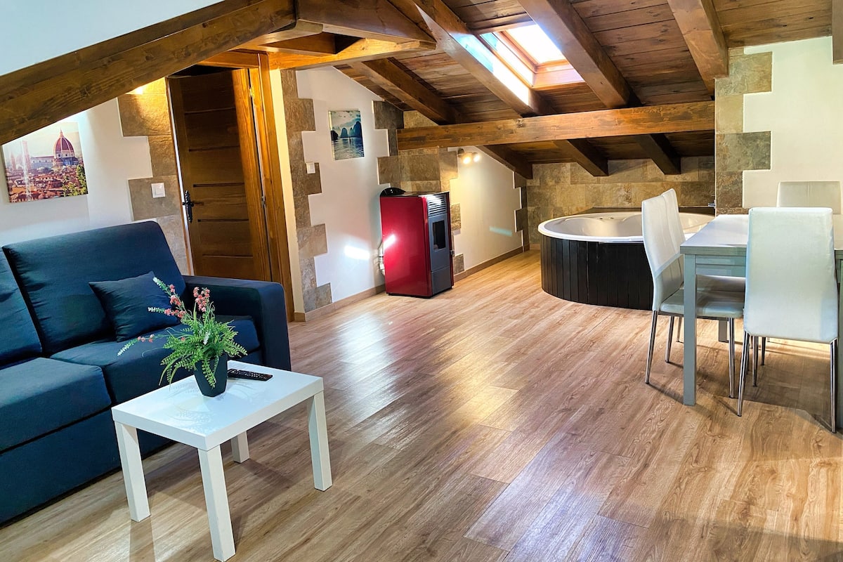 Un acogedor espacio tipo loft con techo de madera, una mesa de comedor con sillas, un sofá, una pequeña mesa blanca con una planta y un refrigerador rojo.