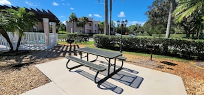 A picnic table with benches, a white fence, and a building in the background.