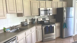 A kitchen with white cabinets, a stainless steel refrigerator, a microwave, a toaster, and an oven.
