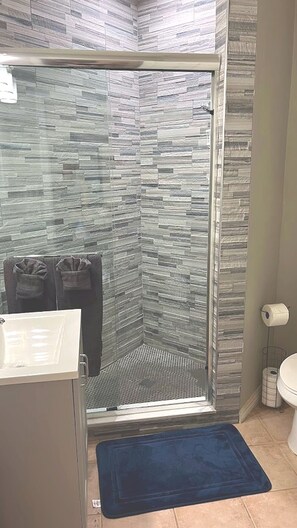 A bathroom with a glass shower enclosure, a sink, a toilet, and a blue bath mat.