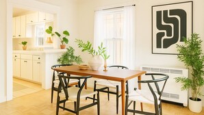 A modern kitchen with white cabinets, a wooden dining table, and black chairs. There are potted plants on the counter and a large black and white artwork on the wall. - Private House/Hollywood Hideaway (West Hollywood)