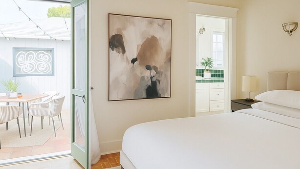 A bedroom with a large bed, a painting on the wall, a desk with chairs, and a view of the outside. - Private House/Hollywood Hideaway (West Hollywood)