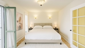 A bedroom with a large bed, two bedside tables with lamps, a ceiling light, and a door with frosted glass panels. - Private House/Hollywood Hideaway (West Hollywood)