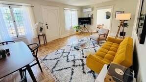 A living room with a sofa, a coffee table, a TV, and a dining area. - Private House/Hollywood Hideaway (West Hollywood)