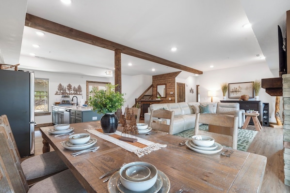 Amplia sala de estar con mesa de comedor de madera para cuatro personas, un sofá y una chimenea.