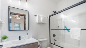 A modern bathroom with a glass shower enclosure, a white toilet, a sink with a mirror above it, and a small potted plant on the counter. - Cozy Cabin with Private Hot Tub, Fireplace & Community Amenities Near Thunder Ridge & Table Rock (Hollister)