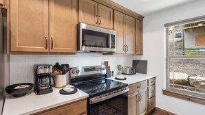 A modern kitchen with wooden cabinets, stainless steel appliances, and a window with a view of the outdoors. - Cozy Cabin with Private Hot Tub, Fireplace & Community Amenities Near Thunder Ridge & Table Rock (Hollister)