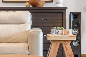 Un moderno salón con un sofá de cuero, una mesa de centro de madera con una taza y pequeñas plantas, un mueble bajo de madera oscura y un altavoz negro.