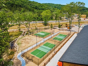 A tennis court complex with multiple courts, surrounded by trees and a small building.
