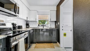 A modern kitchen with stainless steel appliances, white cabinetry, and a large window providing natural light.