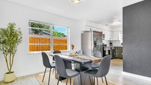 A modern kitchen with a stainless steel refrigerator, white cabinets, and a wooden fence visible through the window.