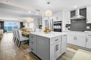 A modern kitchen with white cabinets, stainless steel appliances, and a dining area with a view. - NEW LISTING!!! Sandy Key  823 -8th floor -Beachfront view -NO HASSLE CHECK OUT (Perdido Key)