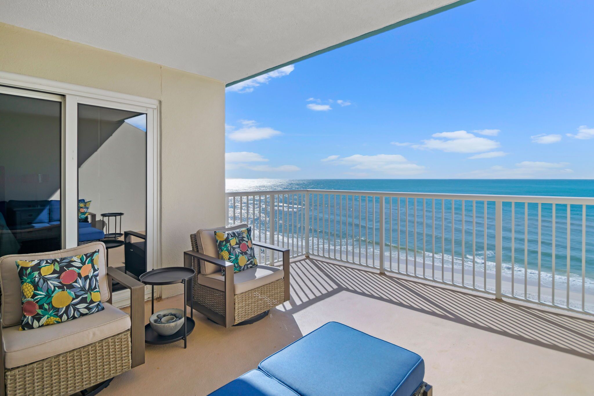 A balcony with a view of the ocean, furnished with wicker furniture and cushions.