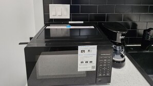 A kitchen with a black microwave, a coffee maker, and a kettle on the countertop. - Bethel Cozy Studio (Edmonton)
