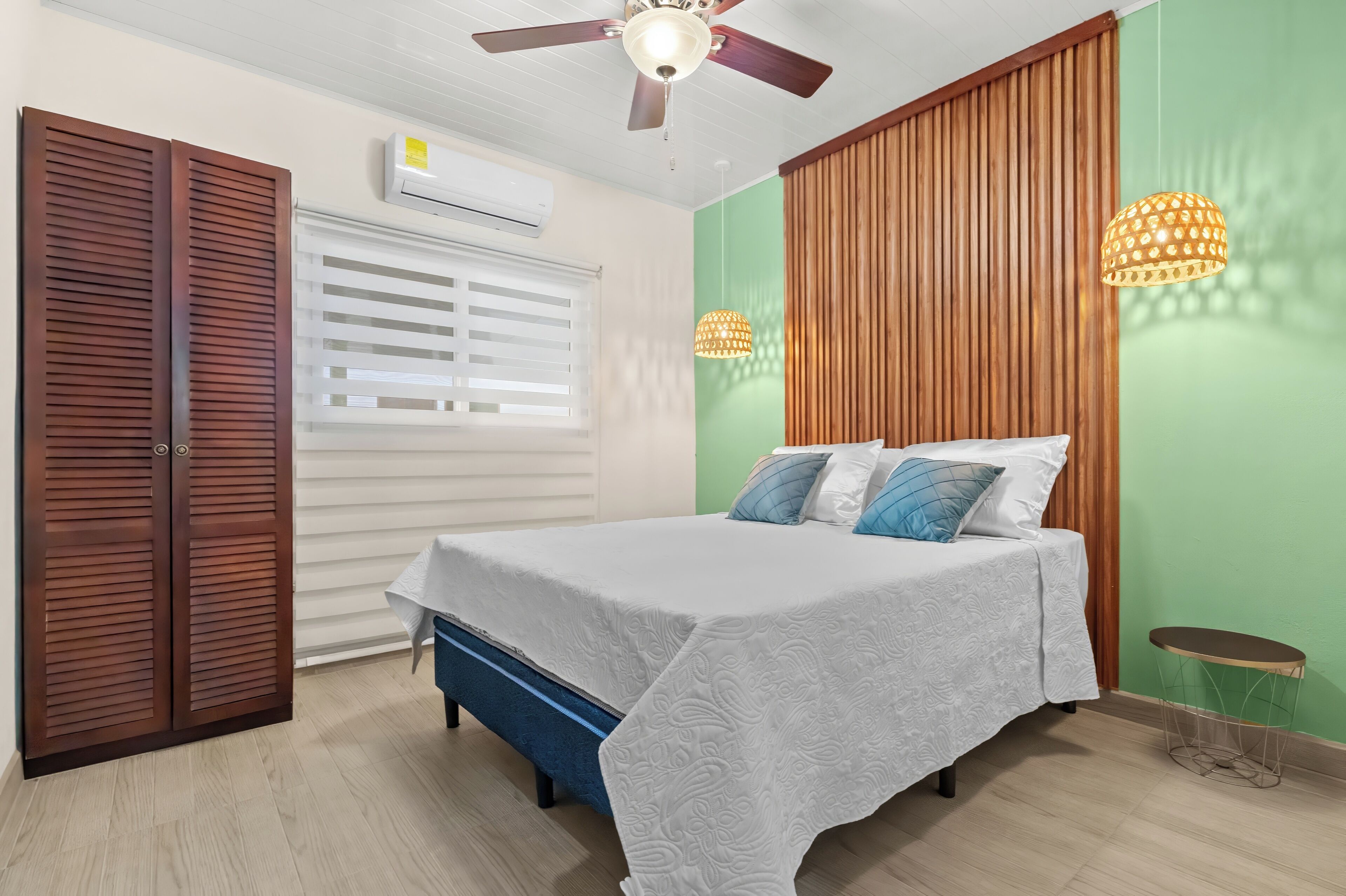 Un dormitorio con cama, armario de madera, unidad de aire acondicionado y ventilador de techo.