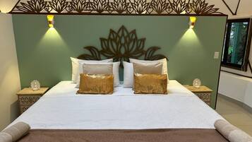 A neatly made bed with white linens and two gold pillows, a decorative wall headboard, and bedside tables with small figurines.