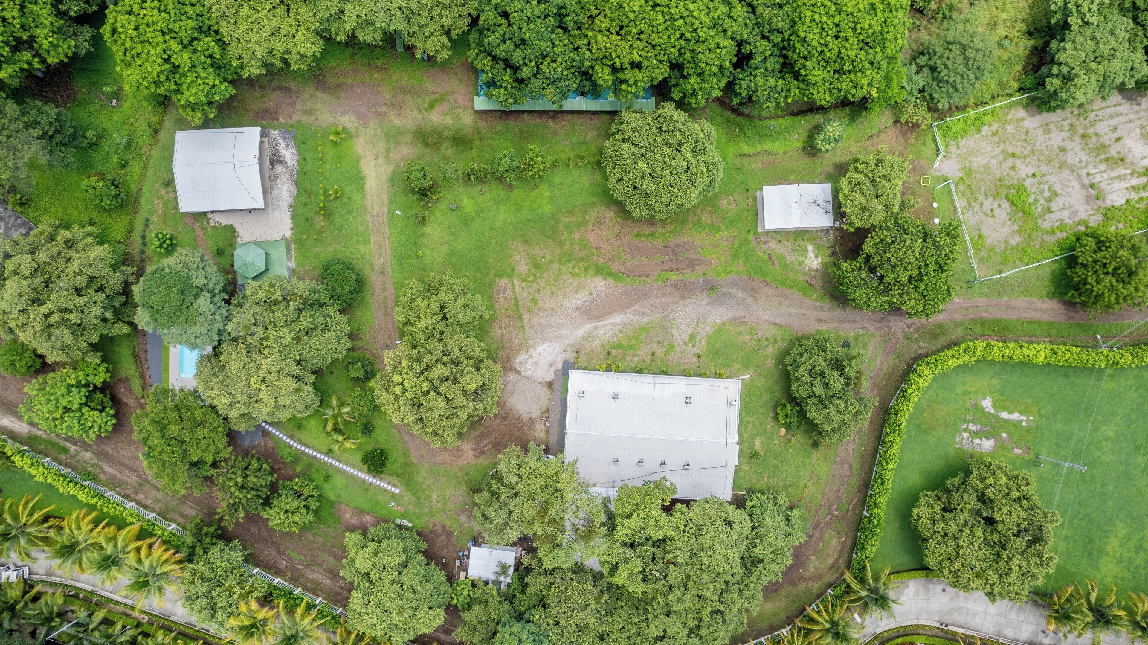 An aerial view of a property with multiple buildings, surrounded by dense greenery and palm trees.