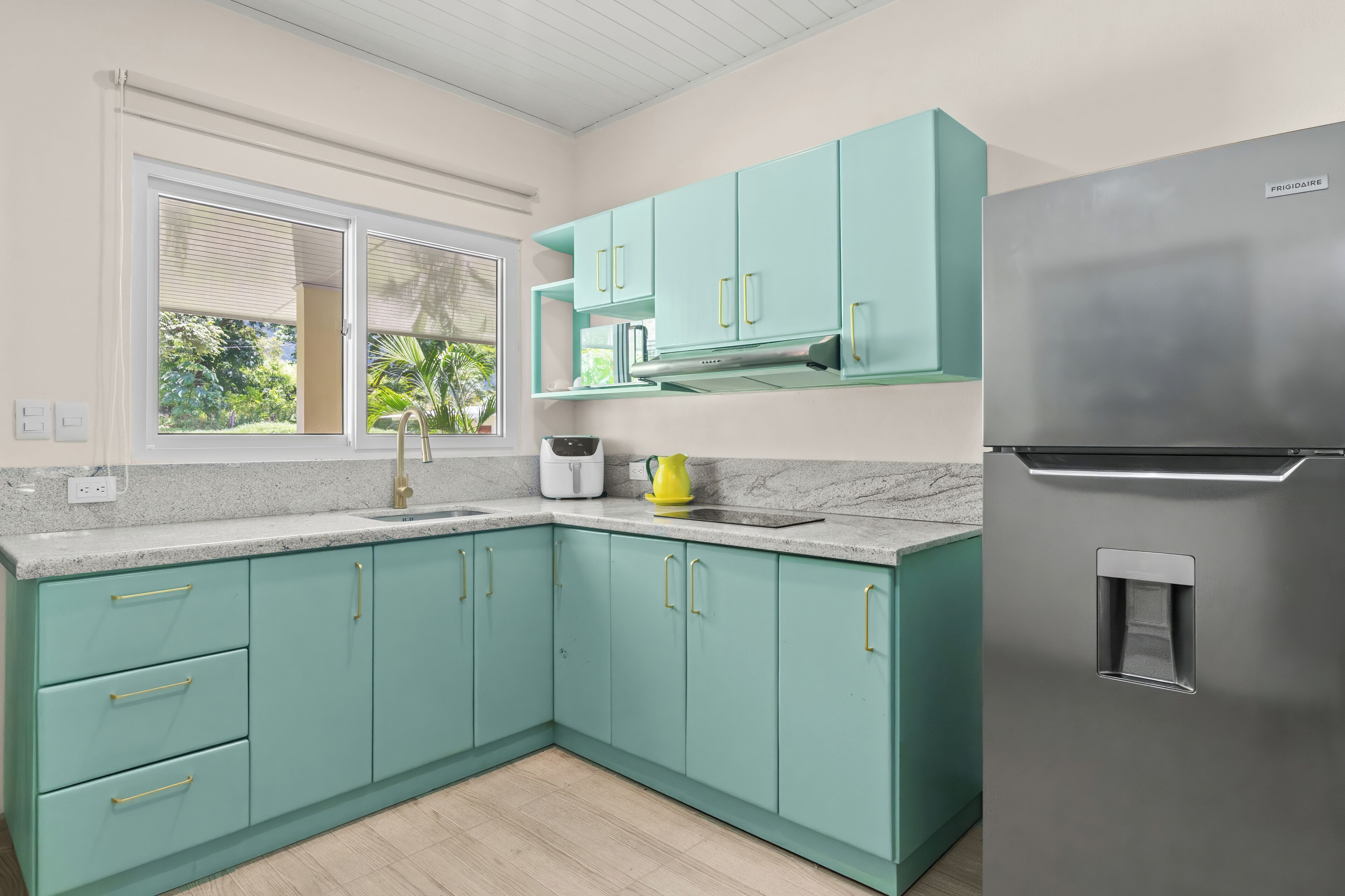 A kitchen with teal cabinets, a stainless steel refrigerator, and a window with blinds.