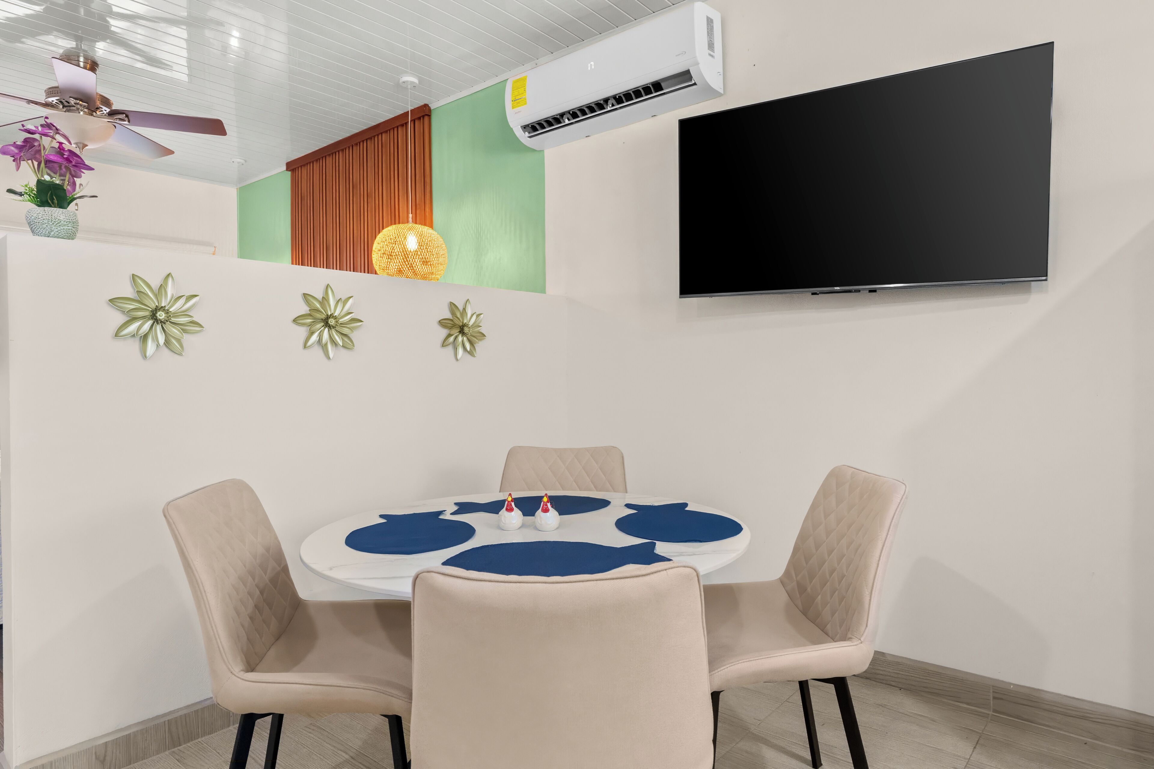 A modern meeting room with a round table, four chairs, a flat-screen TV, decorative wall art, and an air conditioning unit.