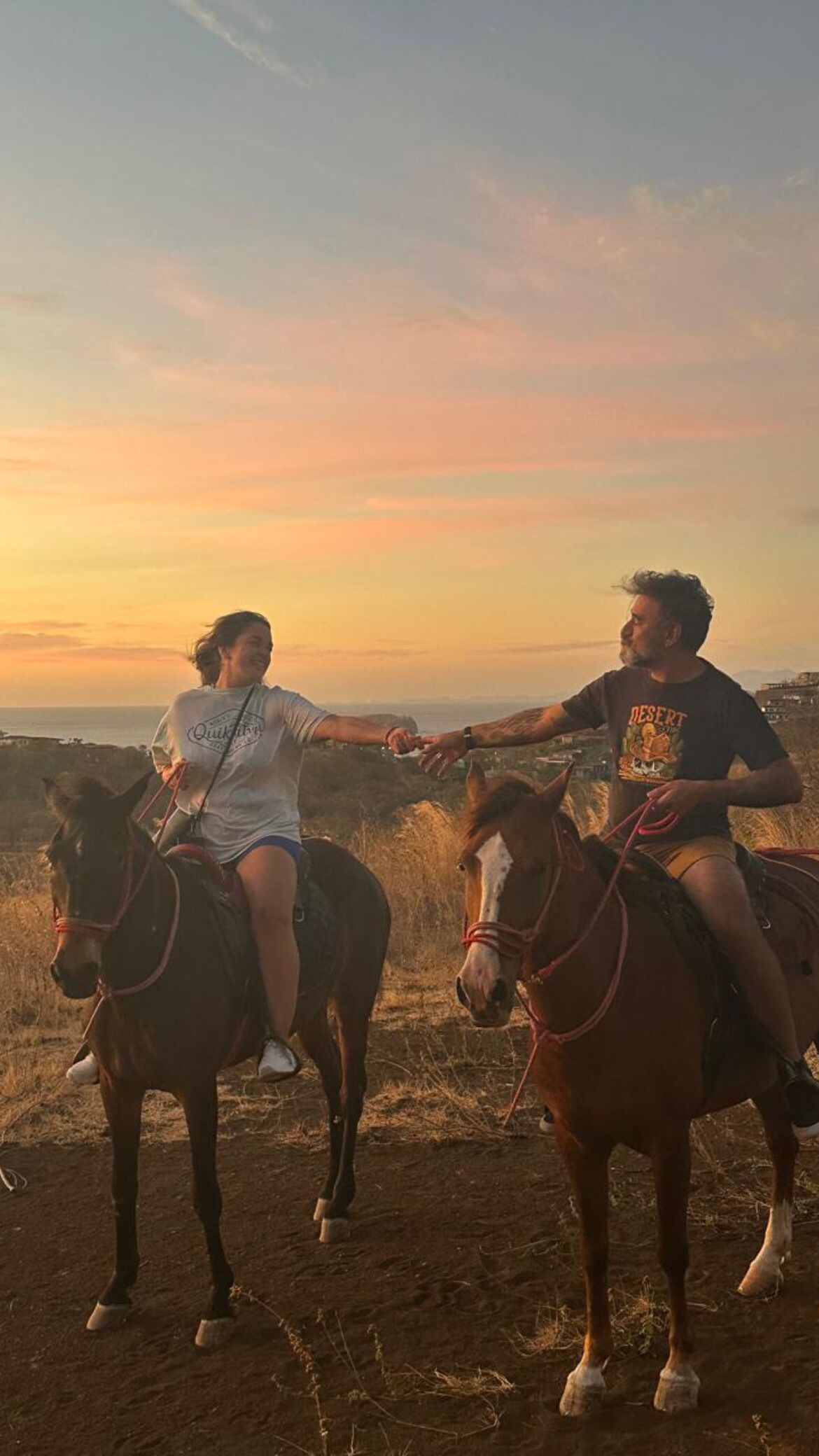 Dos personas montando a caballo en un campo con un atardecer de fondo.