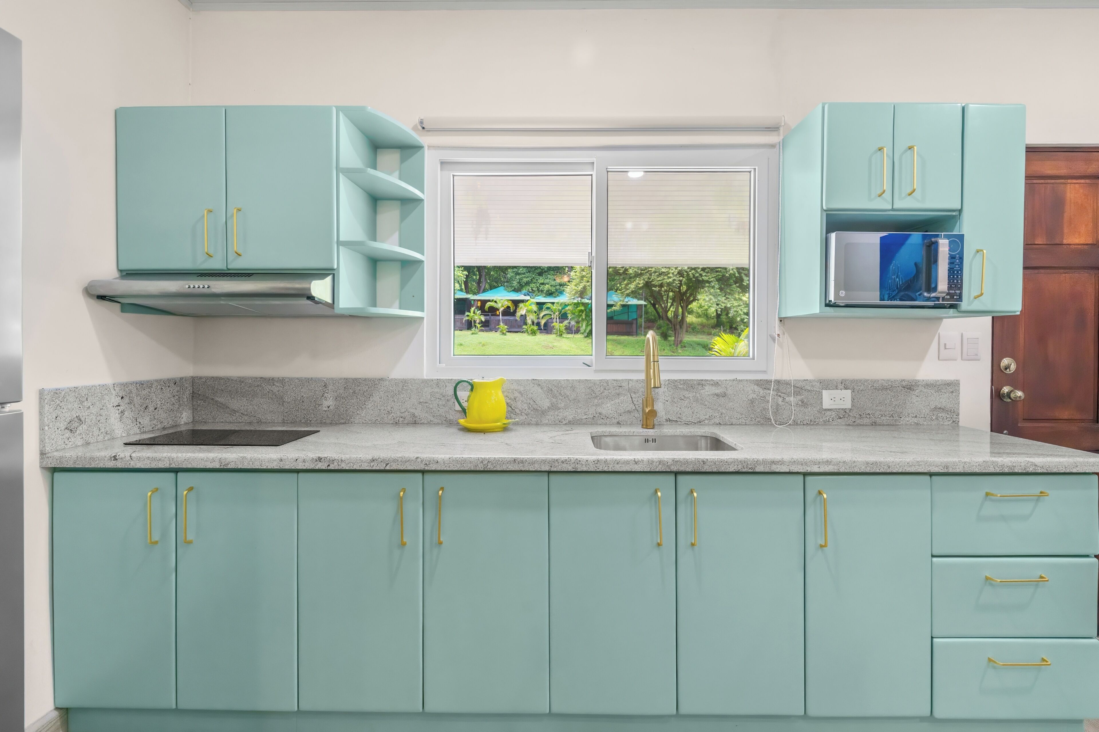 A kitchen with teal cabinets, a double sink, and a microwave.