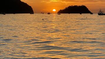 A sunset over a calm sea with boats and distant landforms.