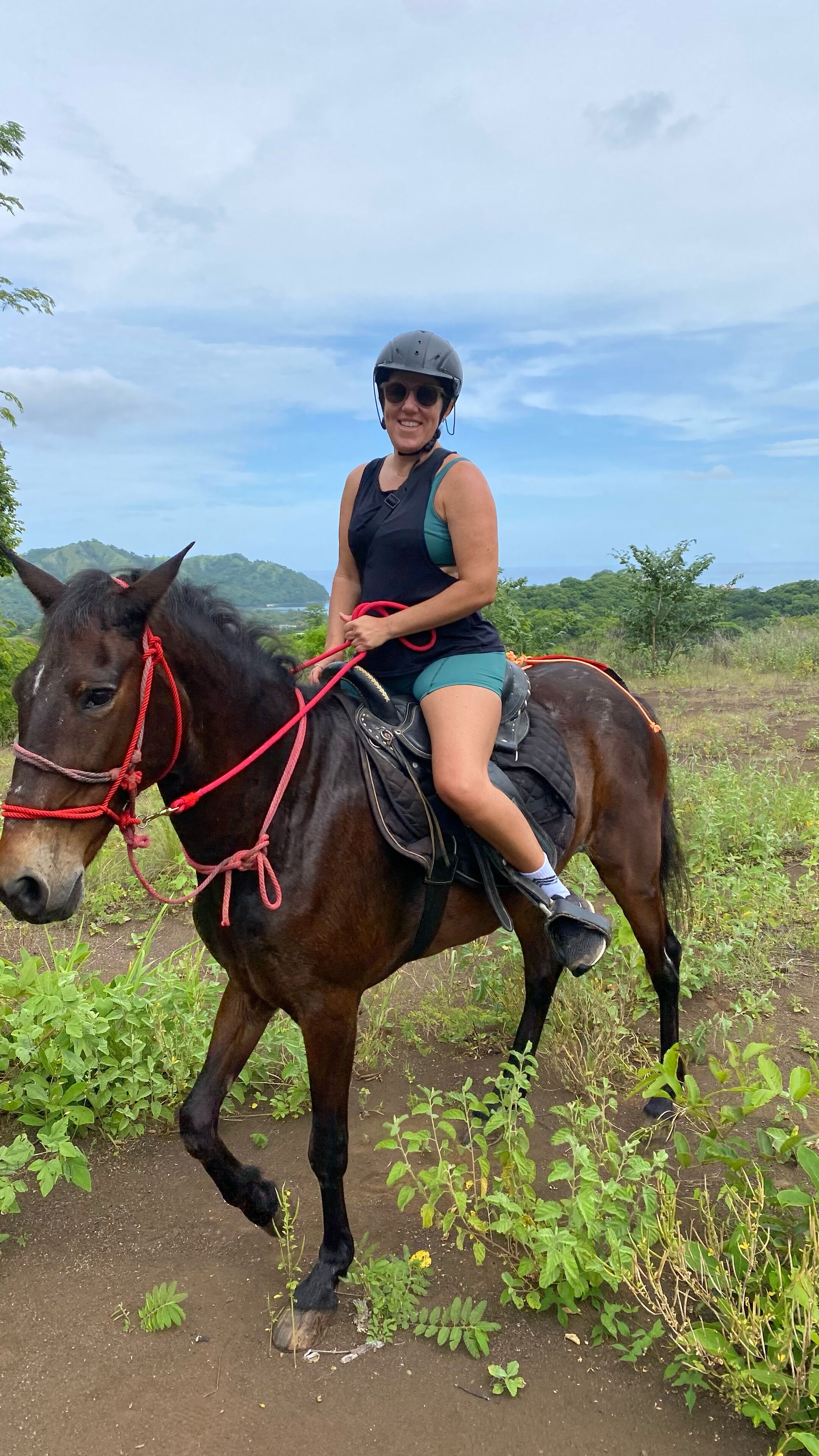 A person riding a horse in a natural setting with greenery and hills in the background.