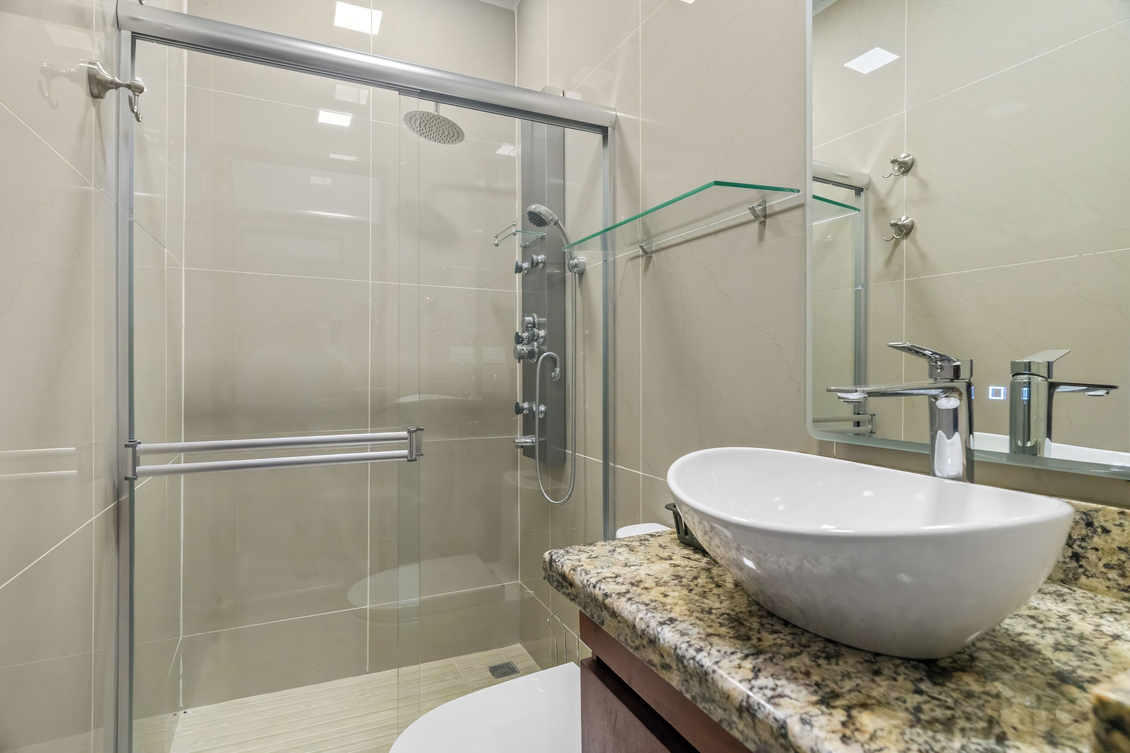 Un bany modern amb dutxa d'acer vidre, un lavabo blanc i un mirall sobre el lavabo.