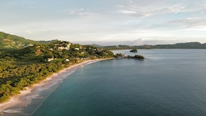 Un paysage côtier avec une plage, une petite île et des collines en arrière-plan.