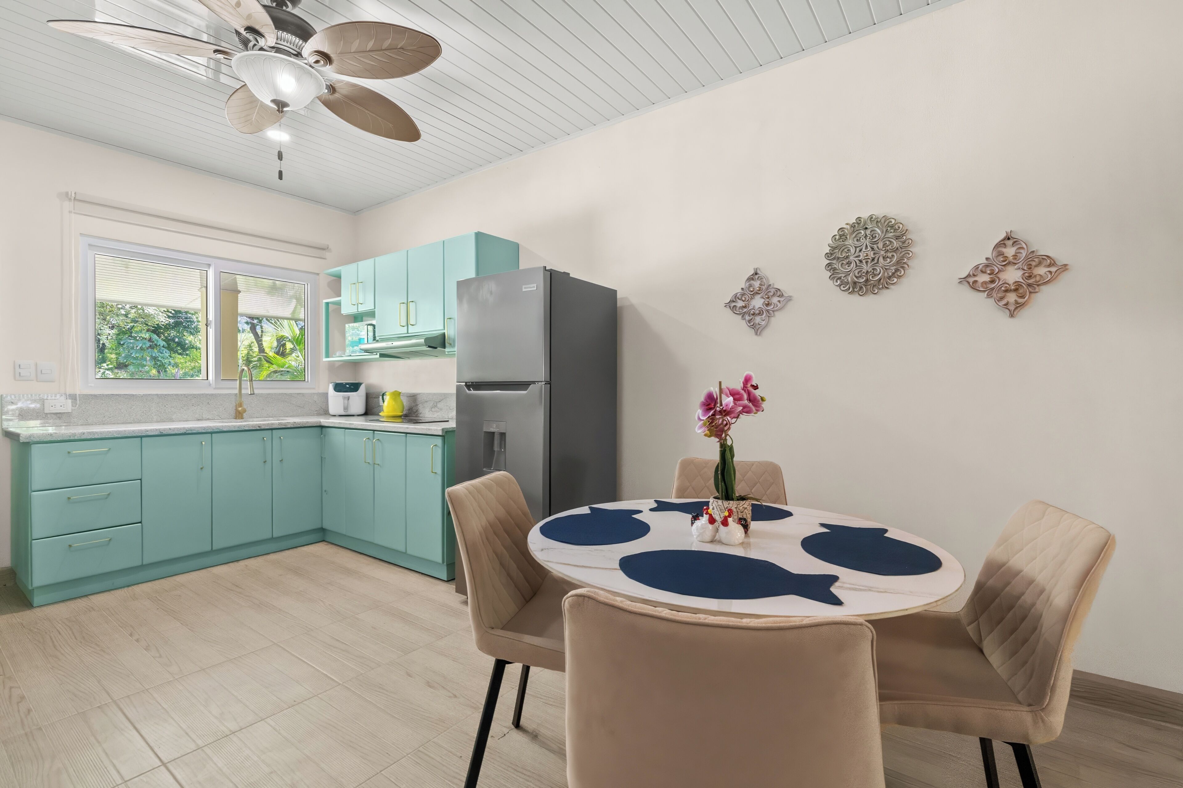 A modern kitchen with teal cabinets, a grey refrigerator, and a dining area with a round table and two chairs.