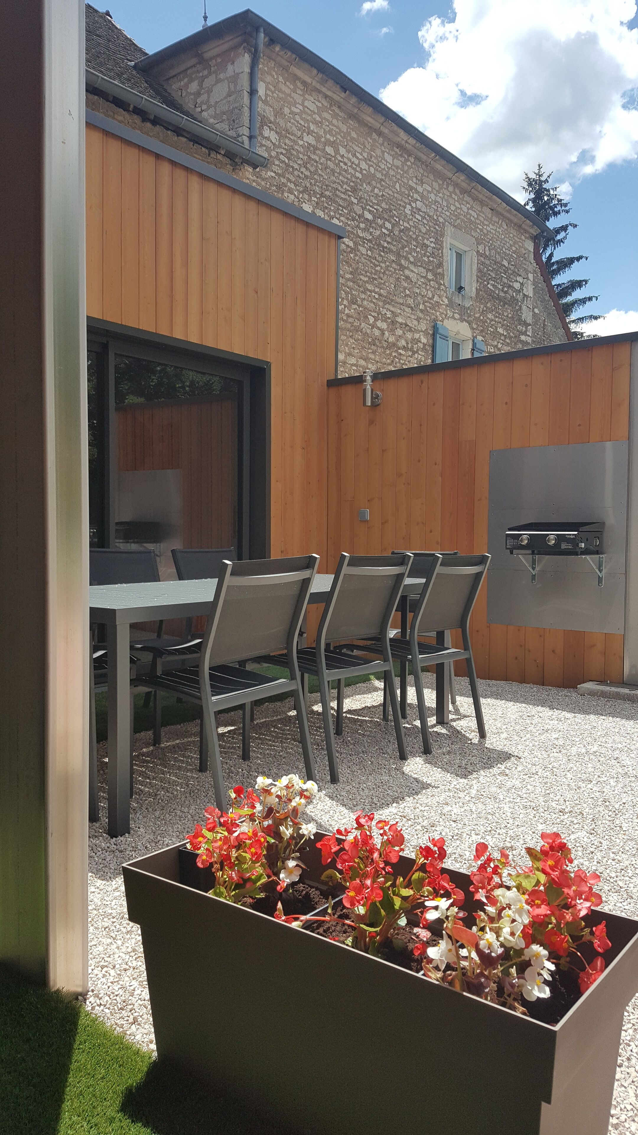 An outdoor patio with a table and chairs, a barbecue grill, and flower planters.