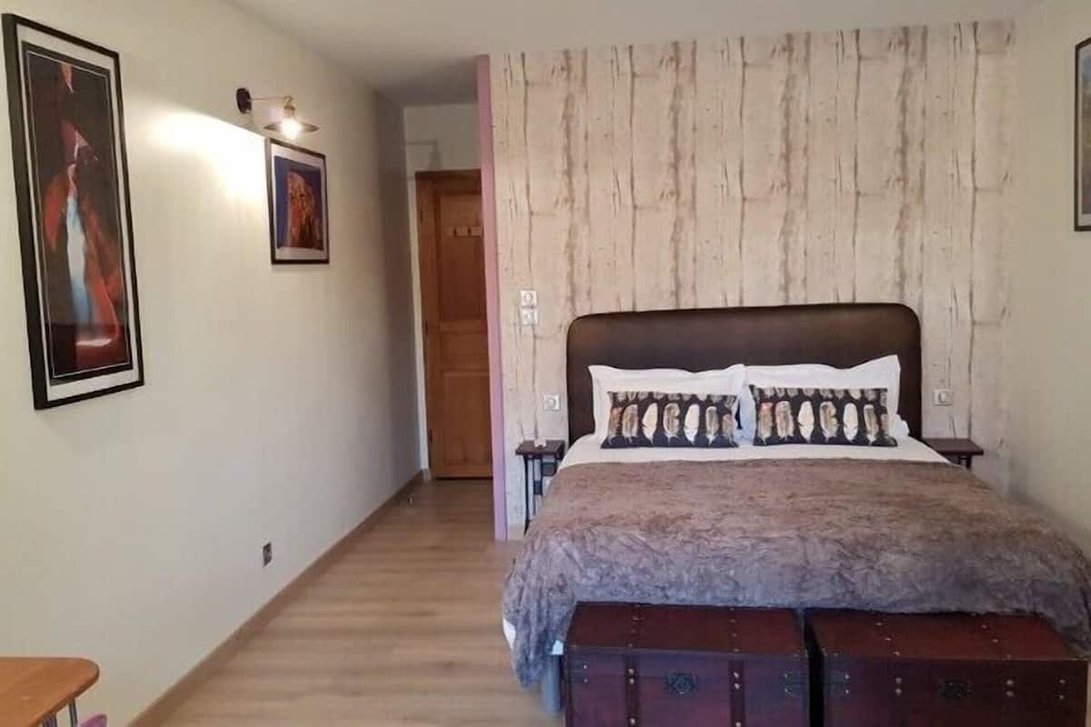 Un dormitorio con una cama grande, piso de madera y una puerta que da a otra habitación.