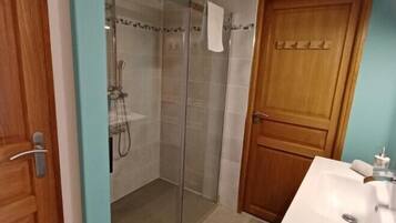 Un baño con cabina de ducha de vidrio, puerta de madera y lavamanos blanco.