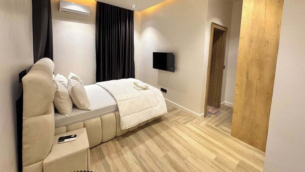 A modern bedroom with a bed, a TV, and a wooden door. - Enclave Hills Hotel (Ibadan)