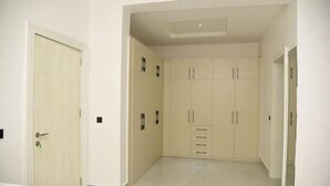 A hallway with a white door, beige wardrobe with multiple drawers, and a tiled floor. - Enclave Hills Hotel (Ibadan)