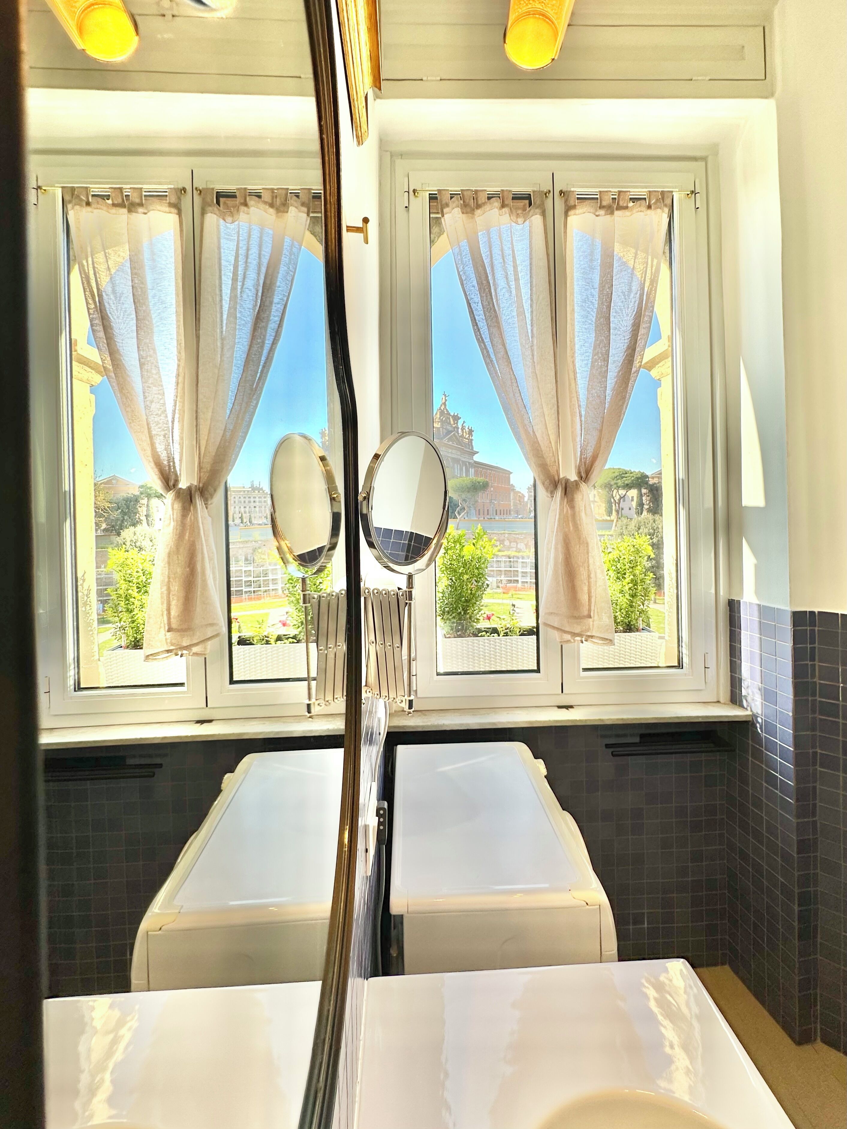 A bathroom with two sinks, a mirror, and a view of a building through the window.