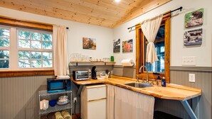 Uma cozinha compacta com bancada de madeira, uma geladeira pequena, uma pia e uma janela com cortinas.