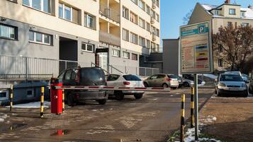 Uma área de estacionamento com entrada por portão, sinalização com as regras de estacionamento e um edifício de vários andares com varandas.