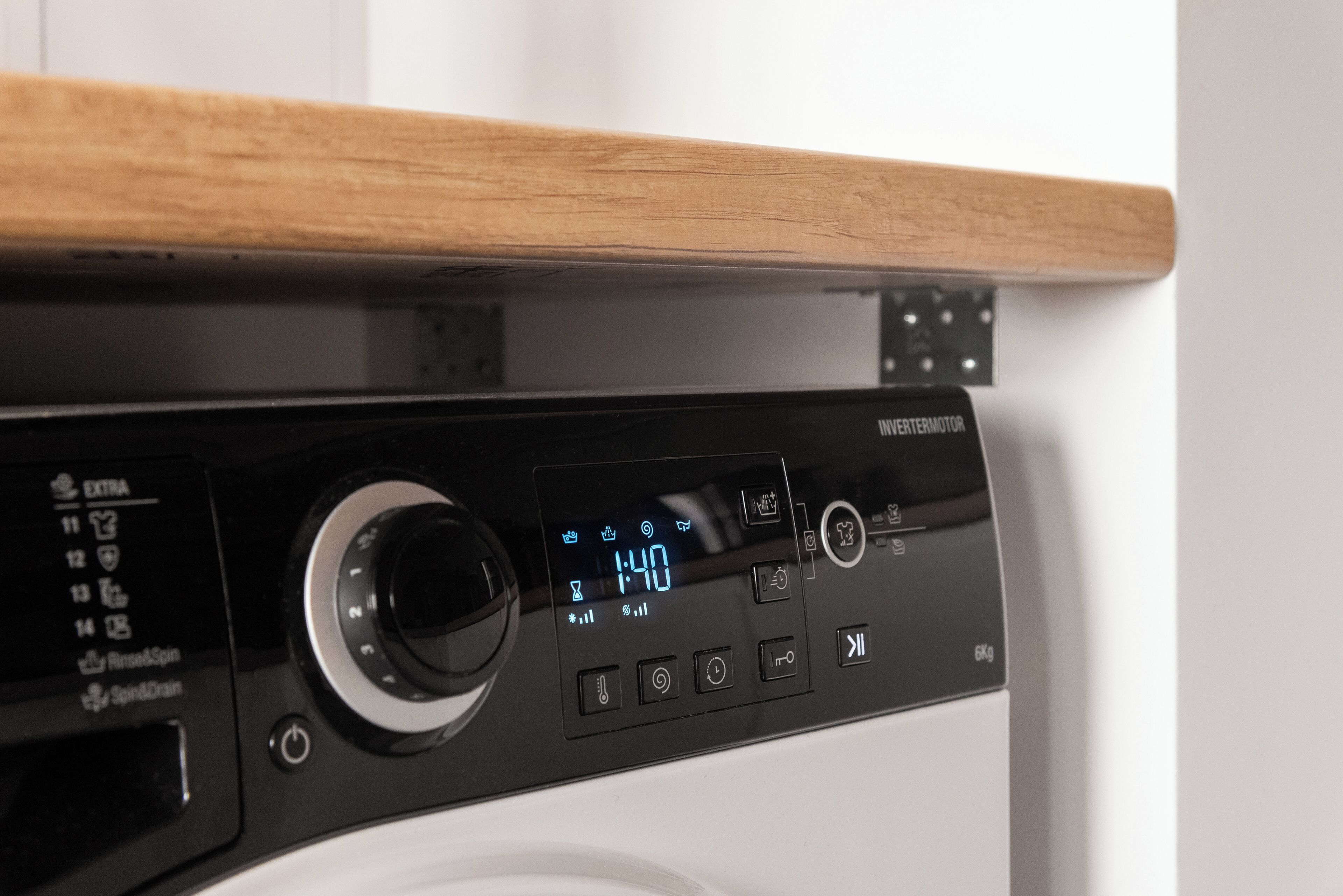 Una lavatrice con display digitale, pannello di controllo e ripiano in legno sopra.