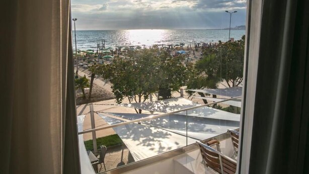 A view from a window overlooking a beach with umbrellas, trees, and a clear sky. - Hotel Besani (Durrës)