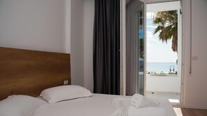 A hotel room with a large bed, white linens, a wooden headboard, and a view of the beach through an open door. - Hotel Besani (Durrës)