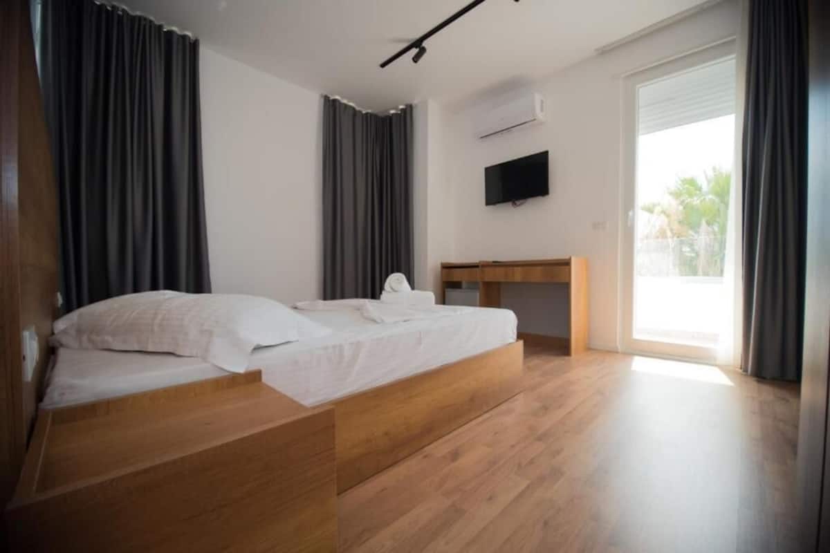 A modern bedroom with a wooden bed, a small desk, and a TV on the wall.