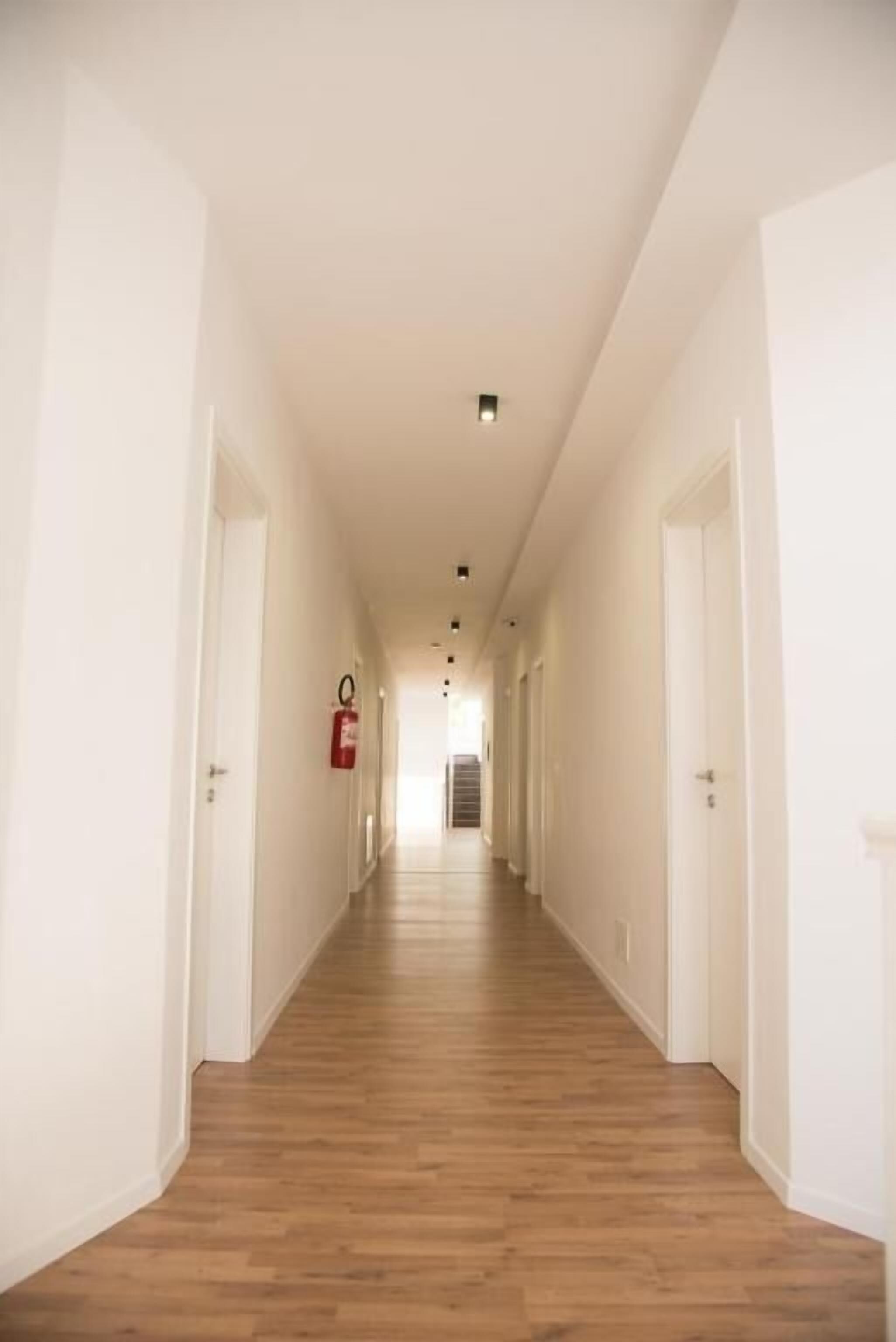Ein langer, schmaler Flur mit Holzdielen und weißen Wänden.