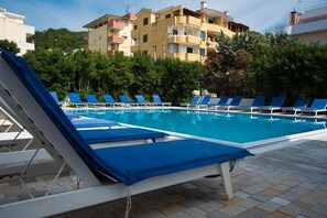 En swimmingpool med blå solstolar och en byggnad i bakgrunden.
