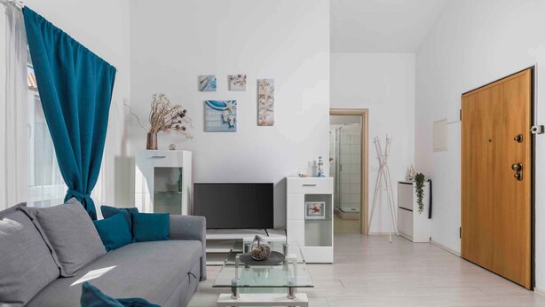 A modern living room with a grey sofa, teal cushions, a glass coffee table, a flat-screen TV, and a white entertainment unit. - Holiday apartment with balcony and air conditioning (Čižići)