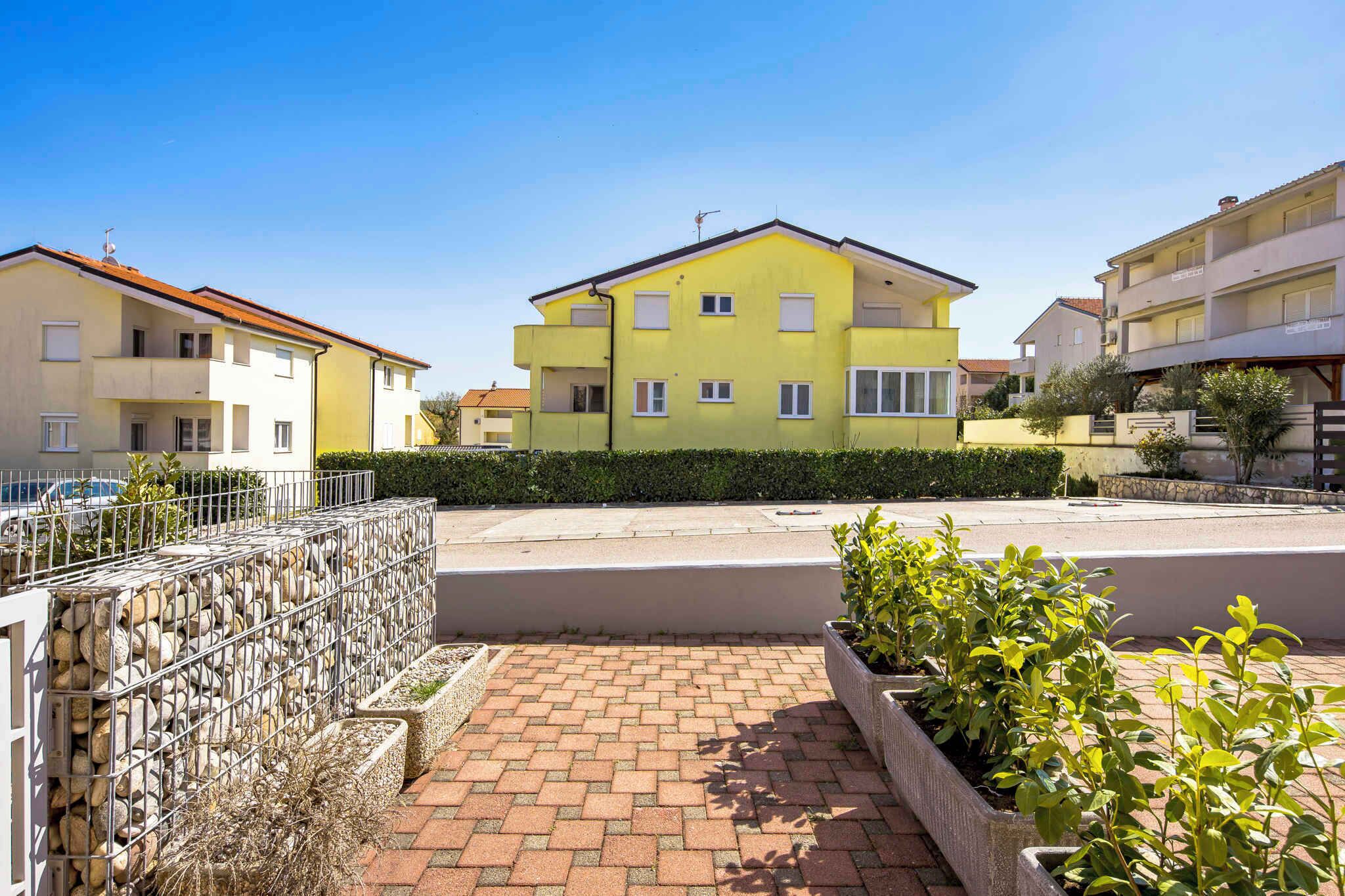 A yellow multi-story residential building with a paved driveway and stone wall.